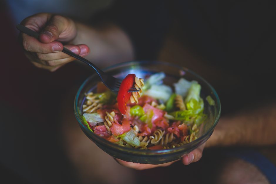 A vibrant bowl of healthy pasta salad with fresh vegetables in a casual setting.