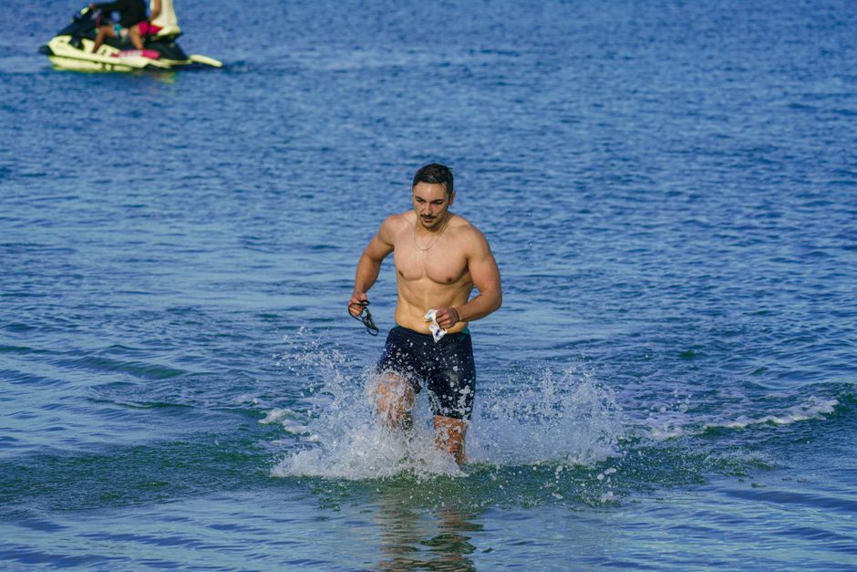 Shirtless man running through shallow water at Kuşadası beach, Türkiye.