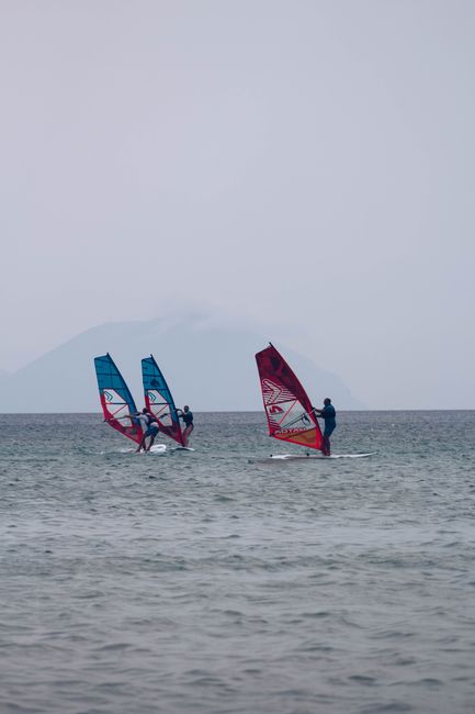 Unrecognizable people balancing on windsurf boards on calm sea water against cloudy gray sky