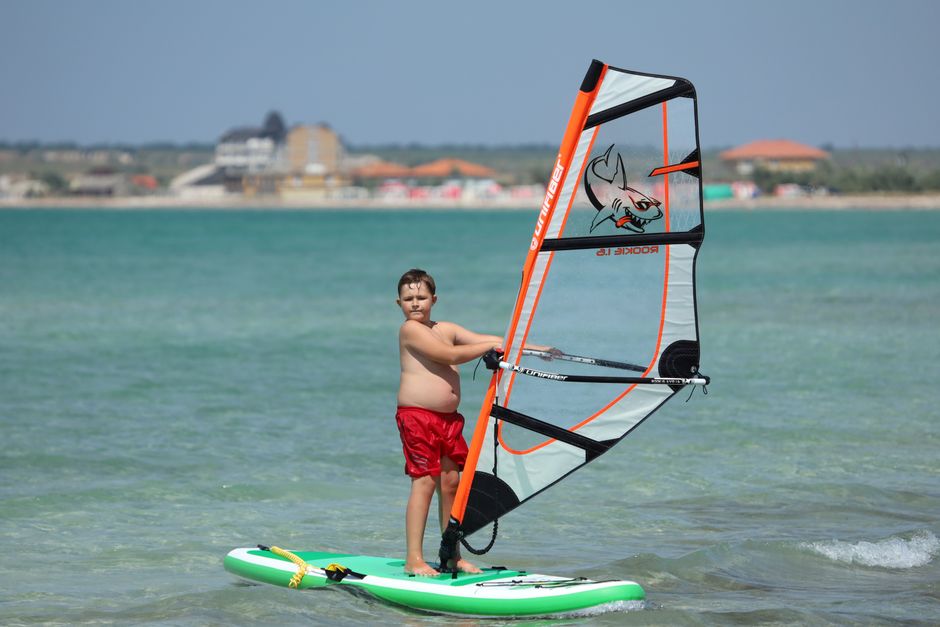 Young boy windsurfing on a sunny beach day, enjoying the adventure sport.