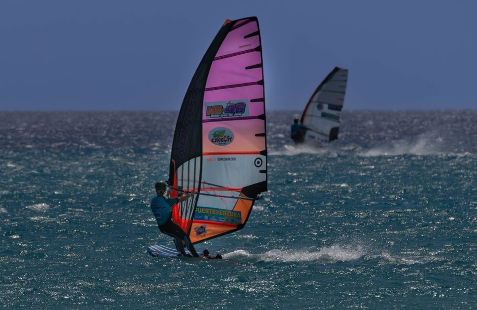 Two windsurfers enjoy the vibrant waters of Fuerteventura under a sunny sky.