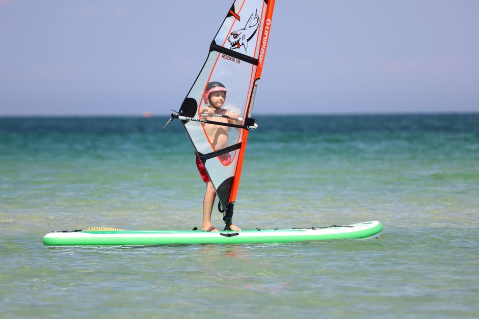 A young boy enjoys windsurfing on clear turquoise waters under a sunny sky.