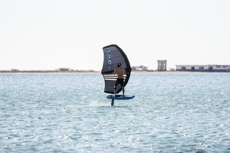 Back view of a man wing foiling on the ocean under a clear blue sky, enjoying water sports.