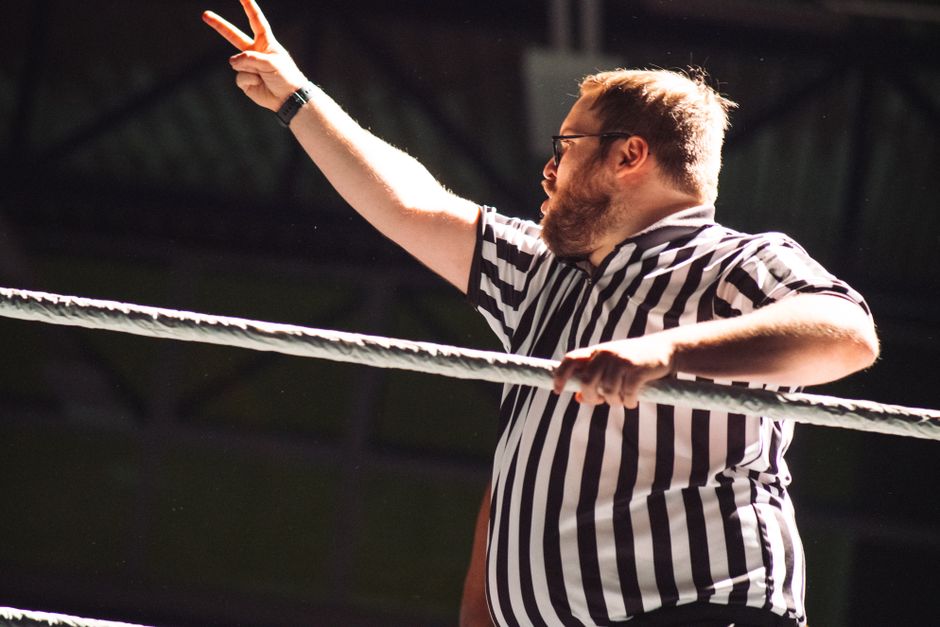 Referee signaling during an intense wrestling match, indoors.