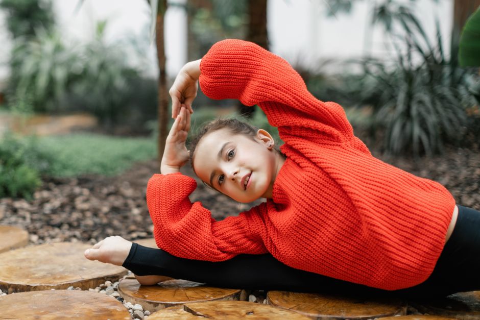 Girl in red sweater doing flexible gymnastics pose outdoors.