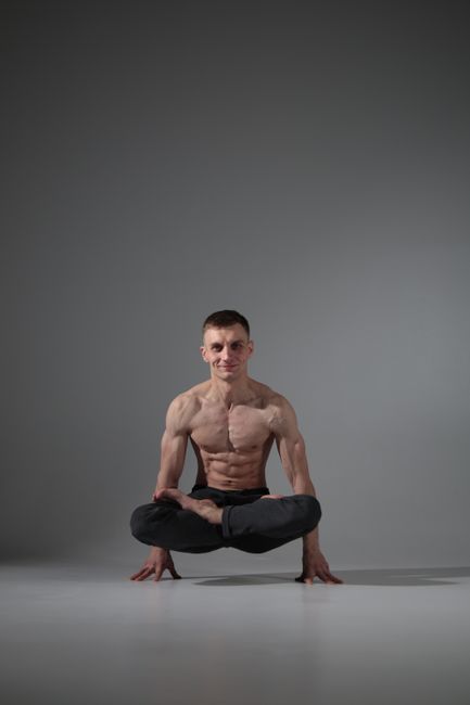 Muscular man performing a yoga pose on a studio floor, showcasing strength and balance.