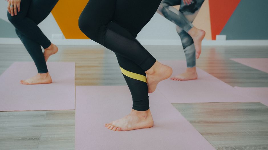 Women performing yoga poses with resistance bands in a modern studio setting.