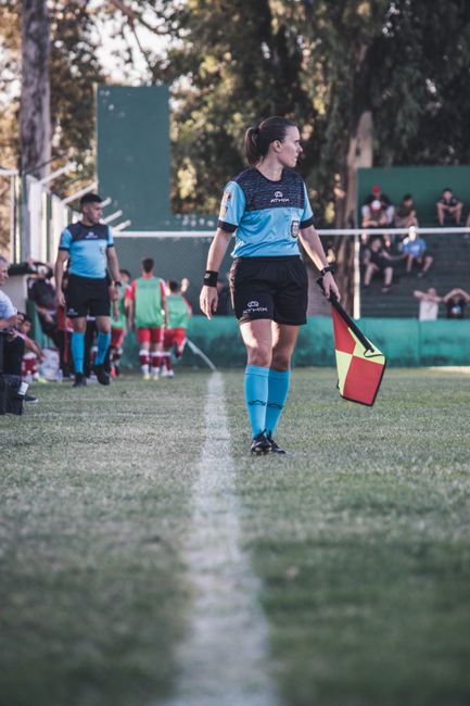 A female referee holding a flag on a soccer sideline, overseeing the match.