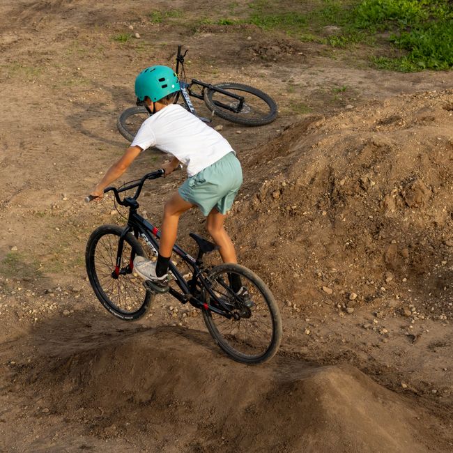 Young boy riding BMX bike on dirt track with helmet, enjoying outdoor adventure.