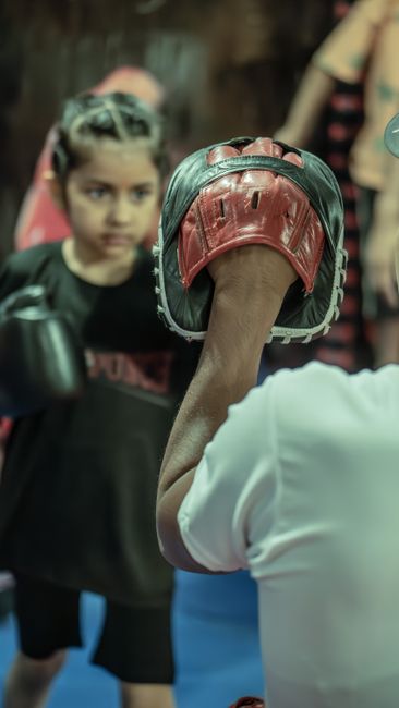 Young girl focused on boxing training with a coach. Dynamic sports scene indoors.