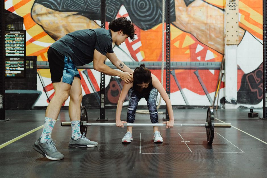 A coach instructs a young woman in proper barbell lifting technique at the gym.