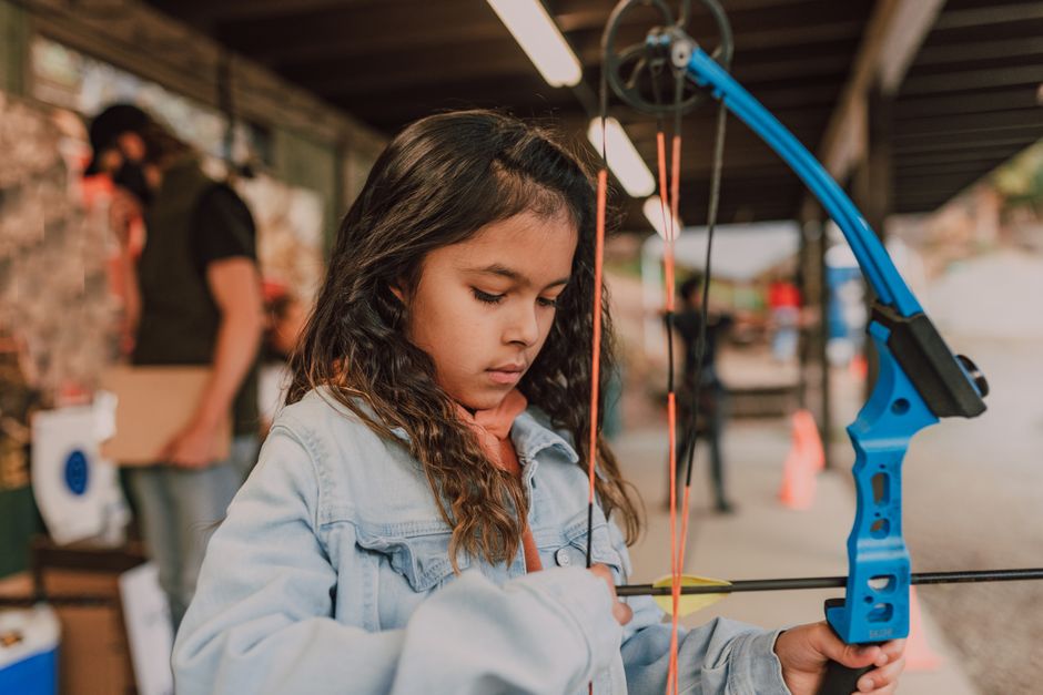 A young girl focusing on her archery skills with a compound bow at an outdoor range.