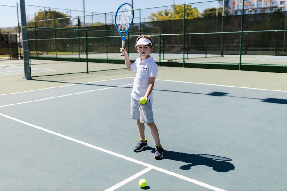 Boy practicing tennis on outdoor court in sunny weather.